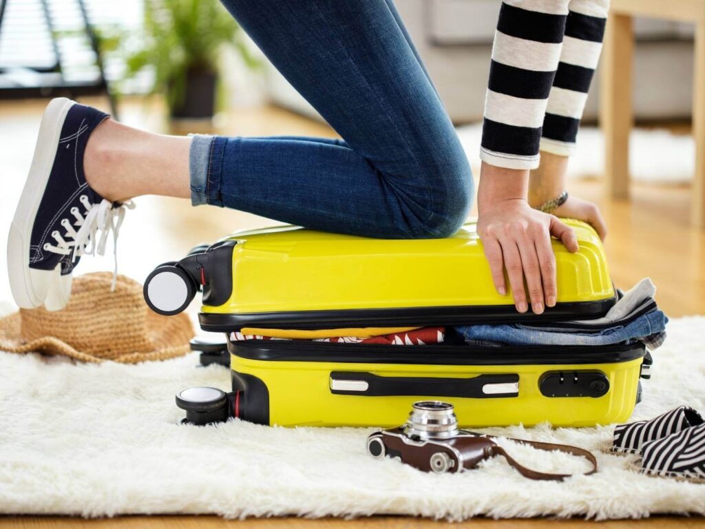 tips for packing a suitcase, Woman trying to close a suitcase