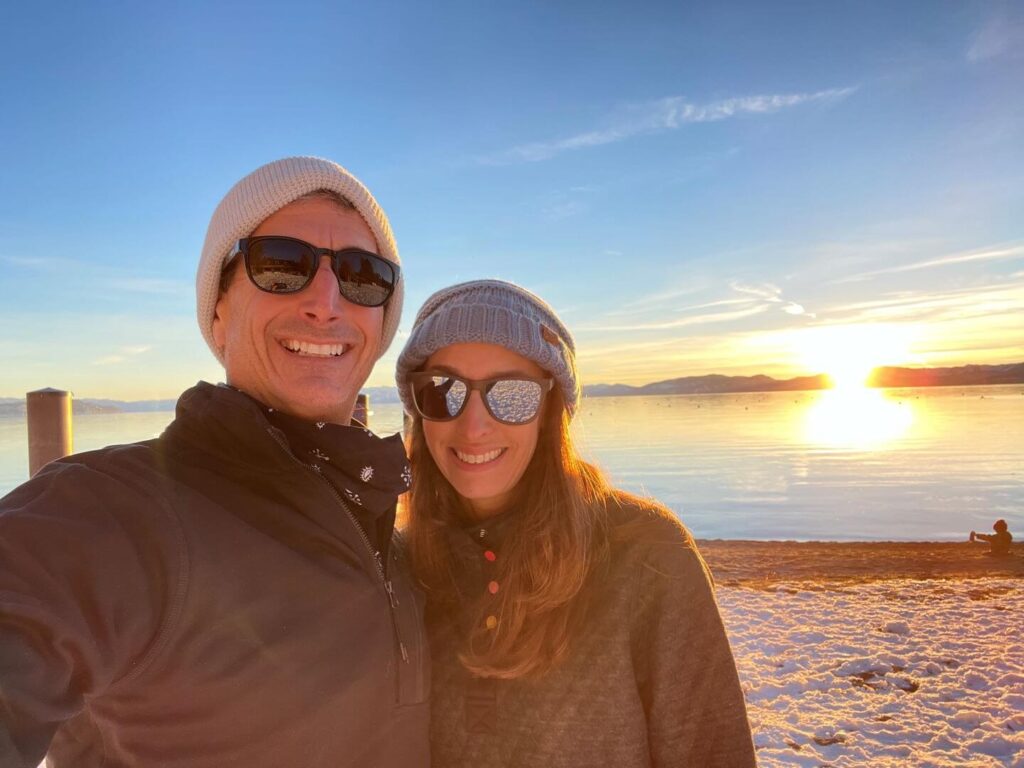 Couple at Lake Tahoe in Incline Village standing on the snowy beach with the sunsetting behind them over Lake Tahoe