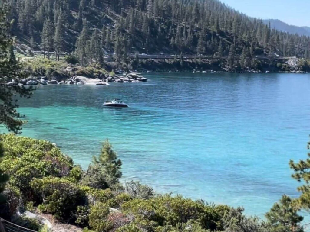 picture of clear Lake Tahoe with trees in the foreground and a boat in the background on the lake