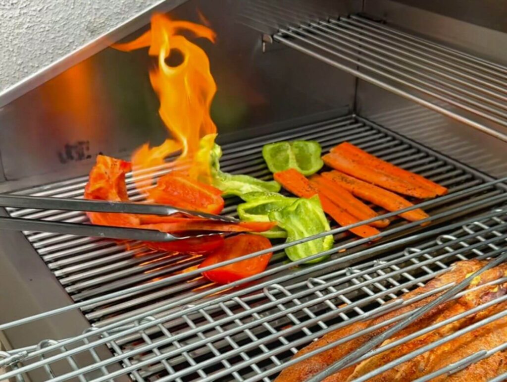 red and green pepers and carrots being fire grilled on an outdoor grill