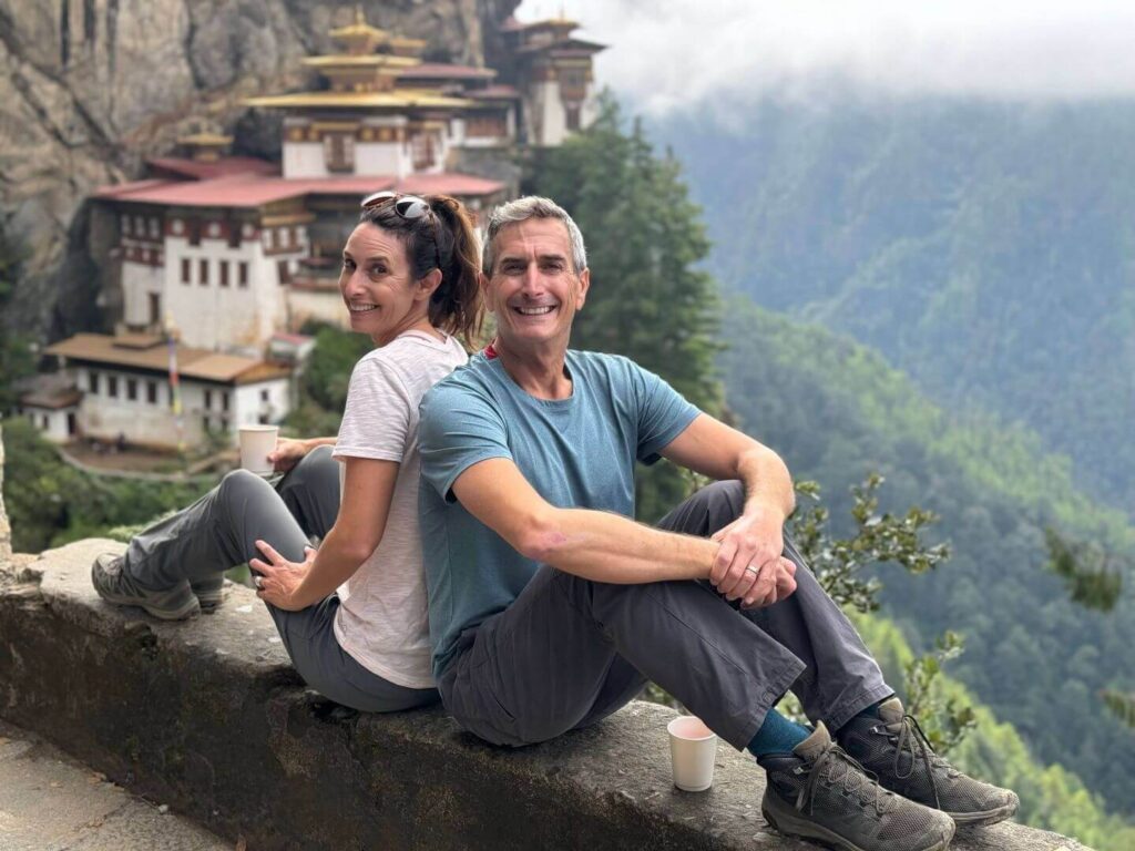 Two people in the forground on a wall with the Tiger's Nest Monestary in the background